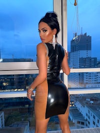 a woman in a black and brown latex dress posing in front of a window